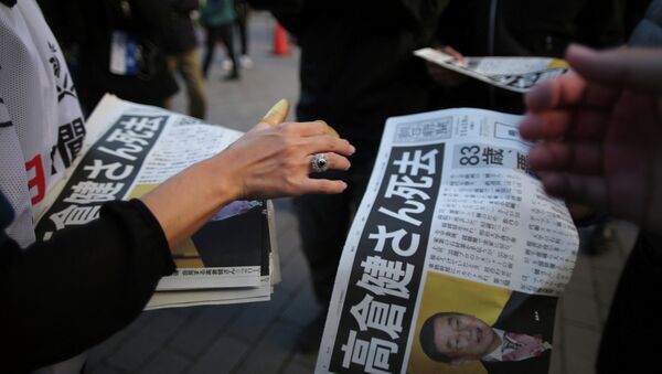 A worker, bottom, distributes an extra edition of a newspaper with front page featuring an obituary notice of acclaimed Japanese film star Ken Takakura at Shimbashi Station in Tokyo, Tuesday, Nov. 18, 2014 - Sputnik Узбекистан