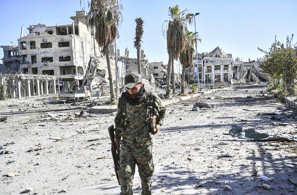 A member of the Syrian Democratic Forces (SDF) walks through a heavily damaged a street leading to an Armenian church in Raqa on October 18, 2017 - Sputnik Узбекистан