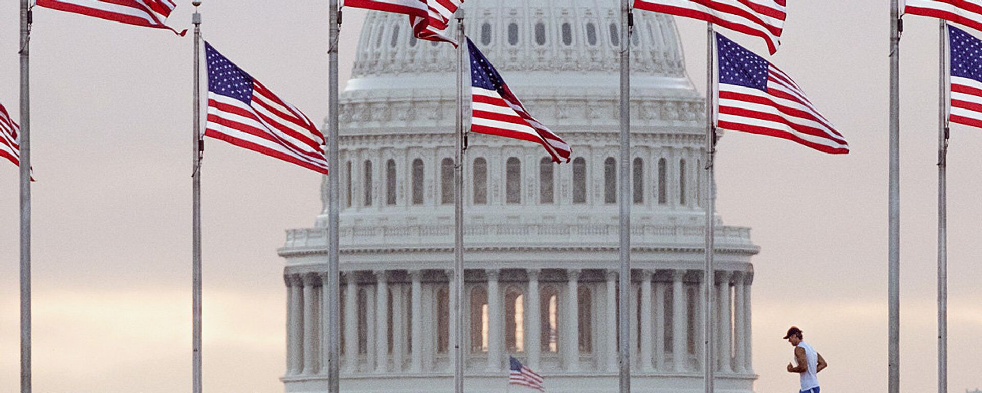 Бегун пересекает площадь перед Капитолием США, проходя мимо флагов, окружающих монумент Вашингтону в Вашингтоне. - Sputnik Узбекистан, 1920, 28.04.2021