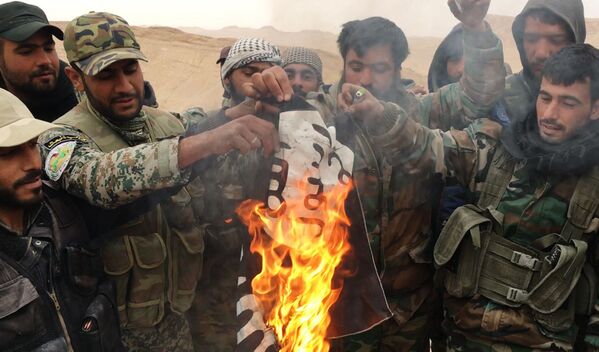 Бойцы отряда народного ополчения Соколы пустыни сжигают флаг запрещенной в РФ организации ИГ, снятый с отбитой у боевиков цитадели Пальмира - Sputnik Узбекистан