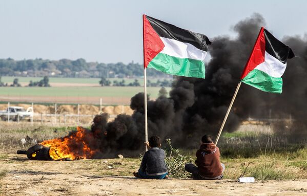 Палестинские демонстранты размахивают национальным флагом у границы между Израилем и сектором Газа - Sputnik Узбекистан