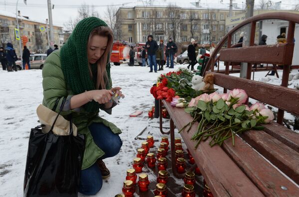 Женщина зажигает свечу возле здания торгового центра Зимняя вишня в Кемерово, где произошел пожар - Sputnik Узбекистан