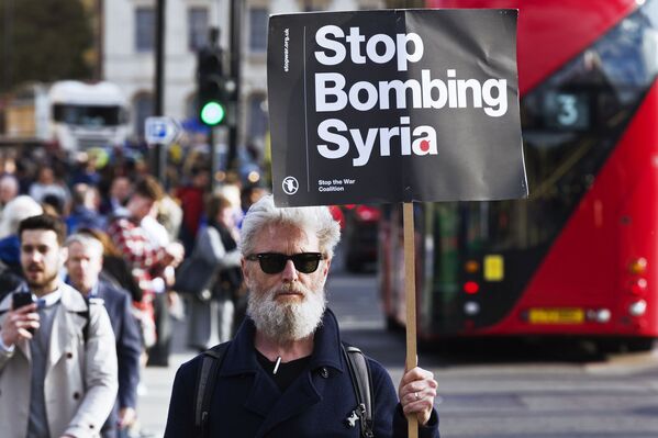 Мужчина держит плакат, призывающий не бомбить Сирию, на акции протеста против ударов по Сирии в Лондоне - Sputnik Узбекистан