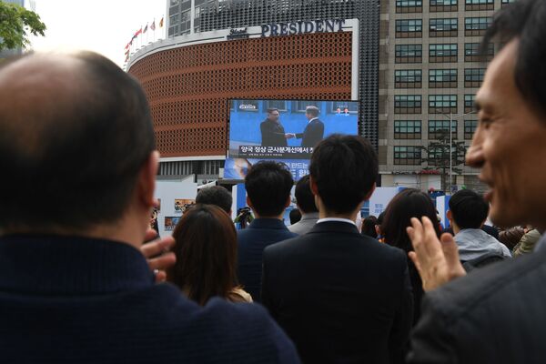 Народ аплодирует, наблюдая на экране в Сеуле за рукопожатием лидеров Северной и Южной Кореи Ким Чен Ына и Мун Чжэ Ина во время их встречи в деревне Пханмунджом в демилитаризованной зоне, разделяющей две Кореи - Sputnik Узбекистан