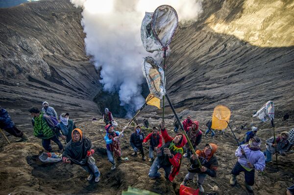 Люди готовятся ловить пожертвования, бросаемые членами племени тенгеров в кратер вулкана Бромо в Индонезии в рамках индуистского фестиваля Yadnya Kasada - Sputnik Узбекистан