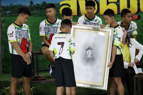 12 спортсменов держат портрет дайвера Самана Гунана, который погиб, спасая мальчиков и их тренера в затопленной пещере на севере Таиланда. - Sputnik Узбекистан