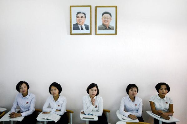 Студенты сидят под портретами северокорейских лидеров Ким Ир Сена и Ким Чен Ира  - Sputnik Узбекистан
